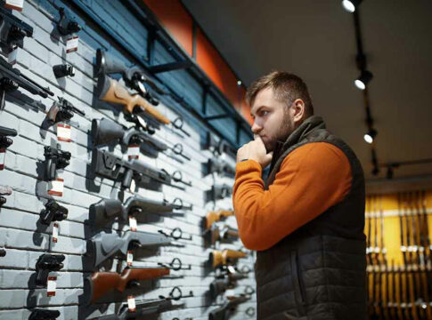 Man contemplating firearms displayed on wall.